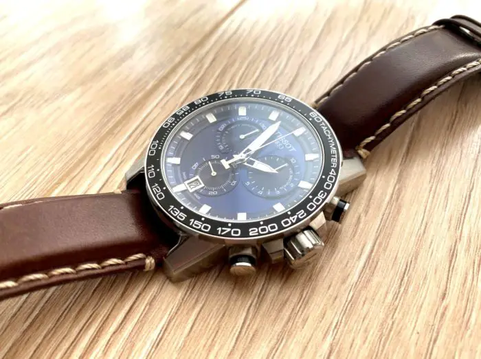 A blue Tissot piece with brown leather strap on a wooden floor